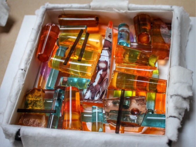 Coloured glass pieces laid into a mould lined with kiln paper. This is the first stage in making a fused glass tile. There is no real way of knowing how it will look when the glass rods and shards melt in the kiln. Image: Su Leslie, 2016